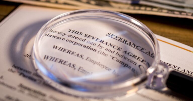 Severance agreement document with magnifying glass. Should you negotiate your severance agreement?